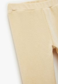 Beżowe legginsy ze żłobieniami wykonane z miękkiego materiału, z elastycznym pasem i gładką fakturą, dobrze dopasowane, bez widocznych elementów wzorniczych.