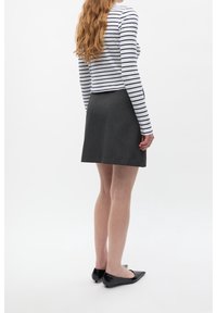 Falda negra en línea A hecha de tela texturizada, combinada con una camisa de rayas blanca y azul marino de manga larga, y zapatos planos negros con punta.