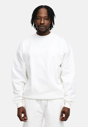 White sweatshirt made of soft cotton, featuring a relaxed fit, crew neckline, and ribbed cuffs. Paired with matching white pants.