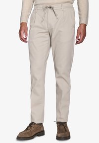 Beige chinos med snøre i taljen. Stoffet er glat. Har forkert plisseringer og tapered ben. Sammen med brune ruskindsko.