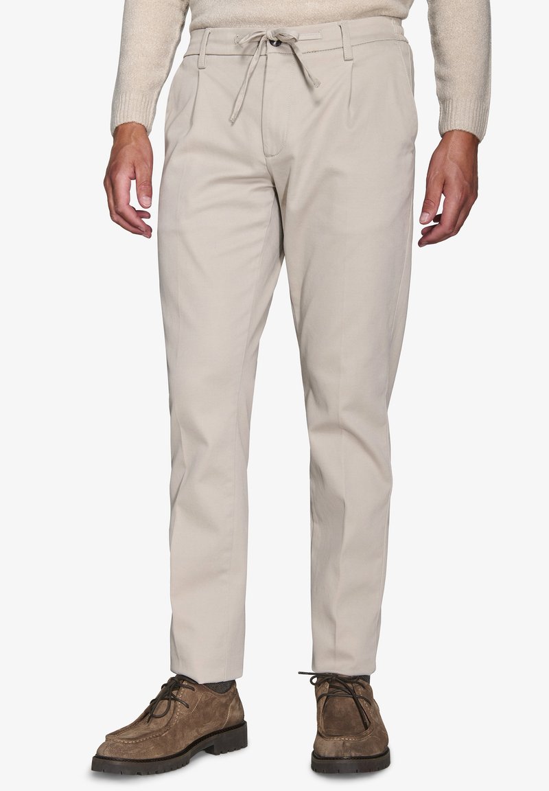 Beige chinos med snøre i taljen. Stoffet er glat. Har forkert plisseringer og tapered ben. Sammen med brune ruskindsko.