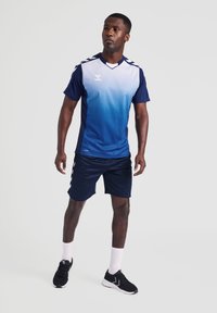 Marineblå og lyseblå sportstrøye med gradientdesign, korte ermer, teksturert stoff, kombinert med matchende marineblå shorts og svarte joggesko.