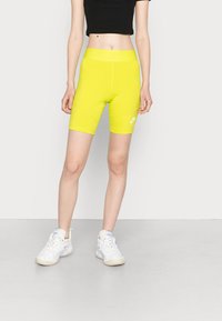 Neon žluté cyklistické šortky s elastickým pasem a logem Nike. Materiál je hladký, střih je přiléhavý. Spárováno s bílými sportovními botami.