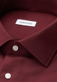 Colletto di camicia in tessuto bordeaux con un'etichetta bianca che recita "seidensticker". Presenta due bottoni bianchi sul colletto, texture liscia.
