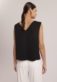 Czarny bezrękawnik z dekoltem w kształcie litery V, o swobodnej sylwetce i gładkiej teksturze, zestawiony z białymi spodniami o wysokim stanie.