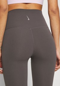 Czarne legginsy Nike z wysokim stanem. Gładki, elastyczny materiał z płaskimi szwami i małym odblaskowym logo na tylnym pasie.