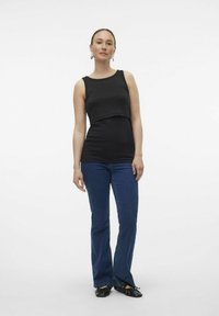 Top negro sin mangas con un diseño corto, combinado con jeans acampanados azules. El top presenta una textura suave y un escote redondo.