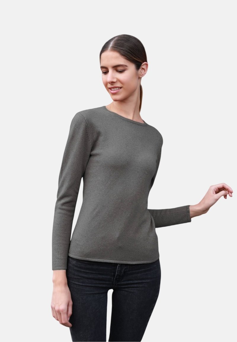 Haut à manches longues gris foncé avec un col rond, fabriqué dans un tissu texturé ; porté avec un jean noir, bras légèrement levés.