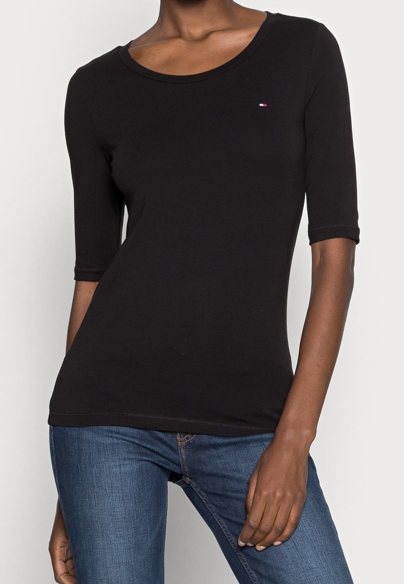 Černé bavlněné tričko s třičtvrtinovými rukávy, kulatým výstřihem a malým logem na hrudi. V kombinaci s modrými džínami.