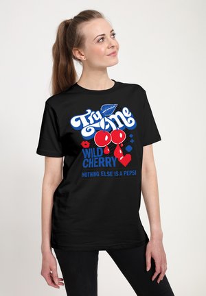 Woman with long ponytail wearing black tee with red cherries and text "Try me wild cherry, nothing else is a Pepsi" looking up.