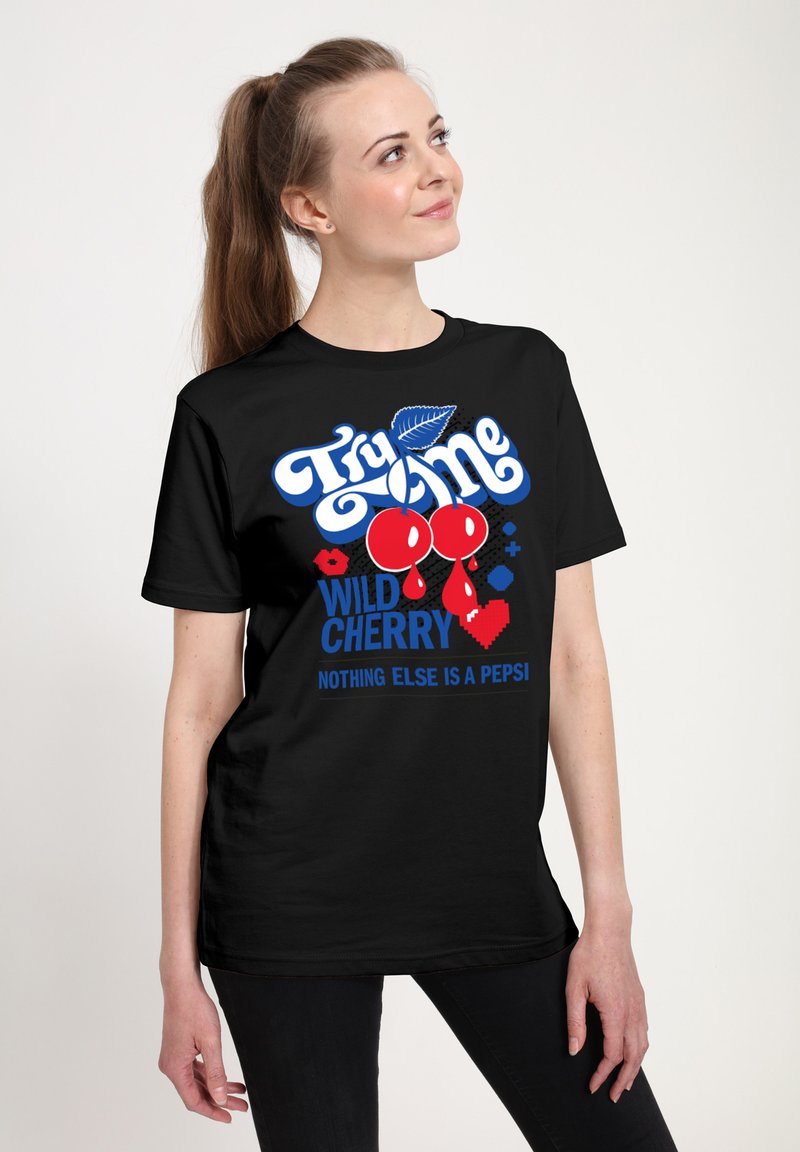 Kvinde med langt hestehale iført sort T-shirt med røde kirsebær og teksten "Prøv mig vild kirsebær, intet andet er en Pepsi" mens hun ser op.