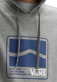 Felpa grigia con cappuccio, caratterizzata da un logo a scacchi blu con testo bianco. Cappuccio regolabile con coulisse e tessuto morbido e strutturato.