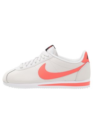 Niskoprofilowy biały sneaker Nike z koralowym logo Swoosh, sznurówkami i akcentami, widziany z zewnętrznej strony na białym tle.