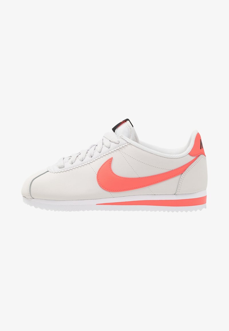 Baskets Nike blanches profil bas avec logo Swoosh corail, lacets et accents, vues de côté extérieur sur fond blanc.