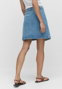 Valkoinen sininen denim A-linjainen hame, jossa on siisti helma, viisi vyölenkkiä ja takataskut, yhdistettynä ruskeisiin litteisiin sandaaleihin.