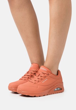 Skechers sneakers in coral, featuring a smooth texture, rounded toe, perforated accents, padded collar, and visible air cushioning.