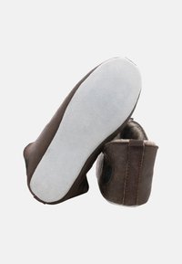 Bruine leren slippers met een zachte beige binnenvoering, voorzien van een ronde neus en een witte, suède-achtige zool. Gestikte details bij de hiel.