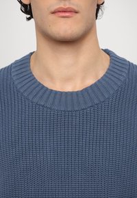 Maglione lavorato a maglia in blu scuro con una trama testurizzata, caratterizzato da un collo rotondo a coste e dettagli morbidi e discreti.