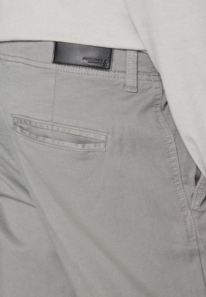 Grijze broek met een gladde textuur, voorzien van een achterzak met een horizontale opening en een klein zwart leren label nabij de tailleband.