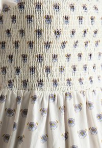 Rochie albă cu volănașe, având un imprimat floral cu accente albastre și galbene. Bustul este texturat prin adunare, iar fusta este lejeră.