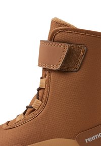 Bota alta marrón con exterior de tejido texturizado, correa de cuero, diseño de cordones y un suave forro de piel en el cuello.