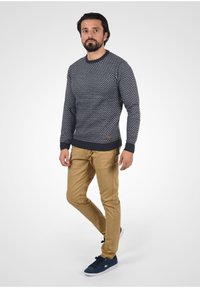 Marine-mønstret sweater med rund halsudskæring, parret med lysebrune chinos og blå sneakers. Sweateren har et struktureret strik og ribstrikkede mansjetter.