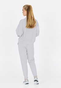 Lichtgrijze oversized sweatshirt en bijpassende joggers, gemaakt van zachte stof, gecombineerd met sneakers met zilveren accenten. Achteraanzicht, eenvoudig ontwerp.