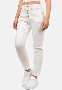 Jean slim blanc à taille haute, avec un devant à cinq boutons, des poches latérales et une texture lisse, associés à des baskets blanches.