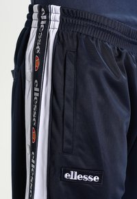 Navy joggers med vit sidremsa, elastisk midja och logopatch. Slät tyg med sidofickor och justerbara funktioner.