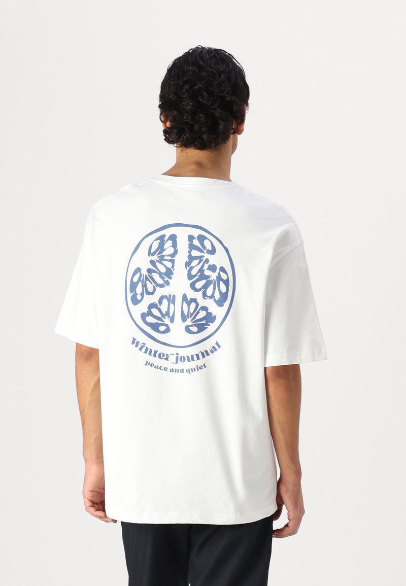 White cotton t-shirt with a large blue circular graphic design featuring floral motifs and the text "winter journal peace and quiet" below.