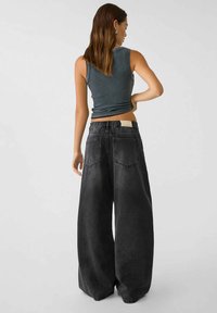 Pantaloni in denim neri a gamba larga con vestibilità rilassata, vita elastica e due tasche posteriori, abbinati a un top smanicato a costine grigio scuro aderente.