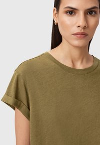 Olivgrünes T-Shirt mit kurzen Ärmeln und umgeschlagenen Säumen, weicher Textur und Rundhalsausschnitt. Nahaufnahme des Stoffdetails und minimalistischen Designs.