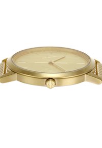 Orologio analogico dorato con un quadrante semplice, lancette sottili e una lunetta testurizzata. Presenta una corona marchiata sul lato, dal design elegante e minimalista.