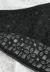 Tissu en dentelle florale noire avec un motif de pétales interconnectés superposé sur un tissu en dentelle blanche avec un design floral similaire.