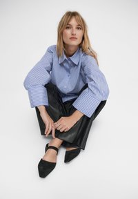 Niebiesko-biała koszula w paski na guziki z dużymi rękawami, zestawiona z czarnymi spodniami z sztucznej skóry i czarnymi płaskimi butami na szpic.