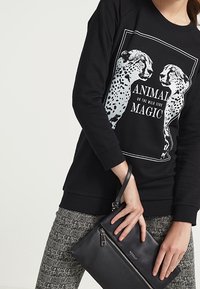 Sudadera negra con gráfico de guepardo y texto "MAGIA ANIMAL", combinada con un bolso de mano negro texturizado. Ajuste casual y cómodo.