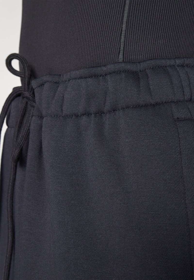 Marineblaue Jogginghosen mit einem Kordelzugbund, die eine glatte Textur und elastische Bündchen aufweisen. Der Stoff erscheint weich und flexibel.