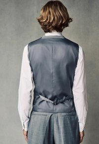Chaleco de satén gris con una textura suave, diseño estructurado y una correa ajustable a juego. Combinado con una camisa de manga larga blanca.