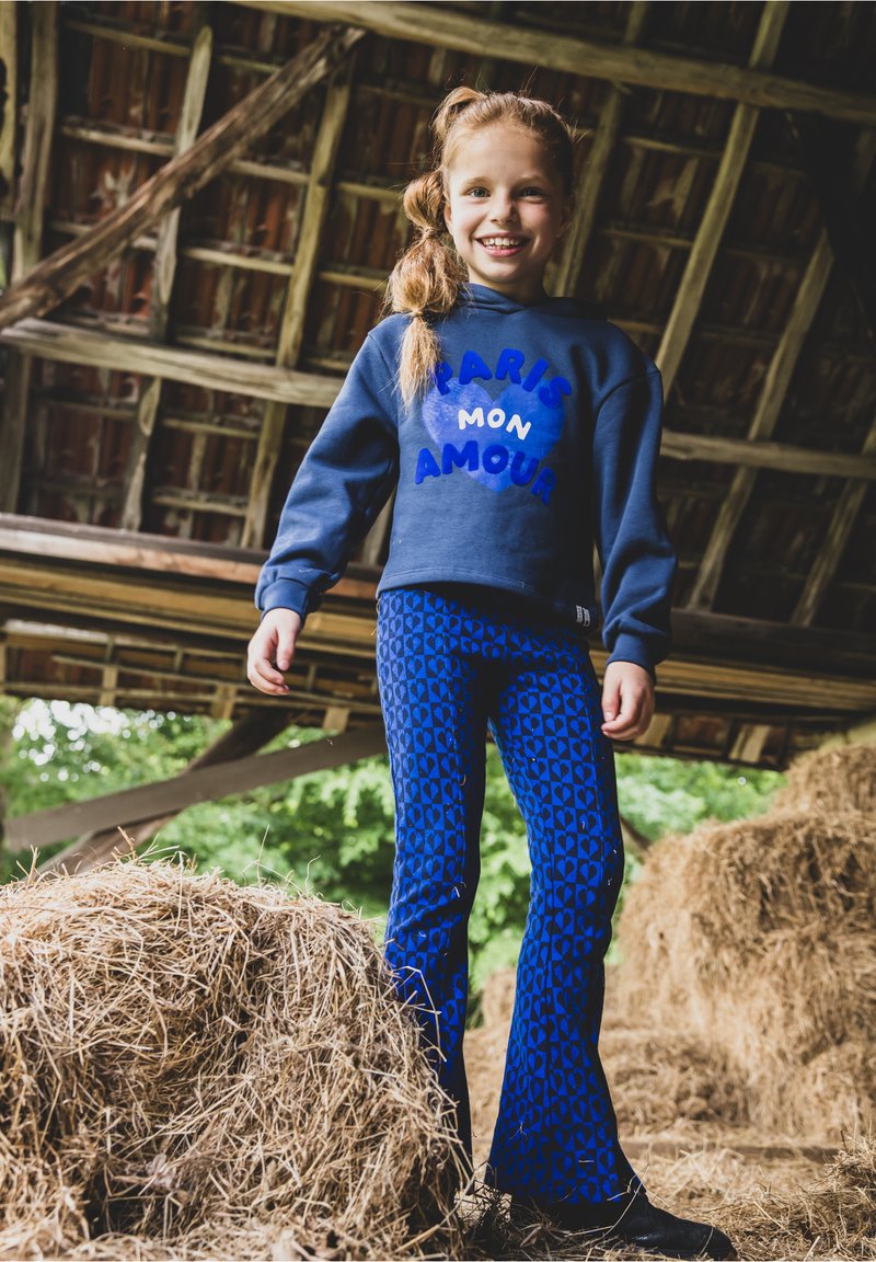 Navy sweatshirt met "PARIS MON AMOUR" in blauw, gecombineerd met blauwe flared leggings met een patroon van hartjes. Zachte katoenen textuur.