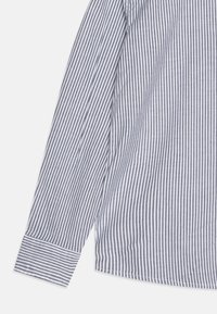 Camicetta a maniche lunghe a righe in blu navy e bianco. Caratterizzata da un colletto classico, polsini con bottoni e tessuto testurizzato con righe verticali uniformemente distribuite.