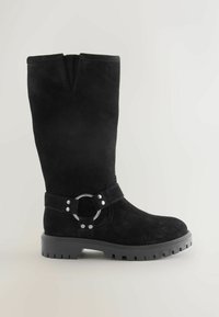 Zwarte suede kniehoge laars met een ronde metalen ringaccent en een gespband. Dikke zwarte rubberen zool met een geribbeld patroon.