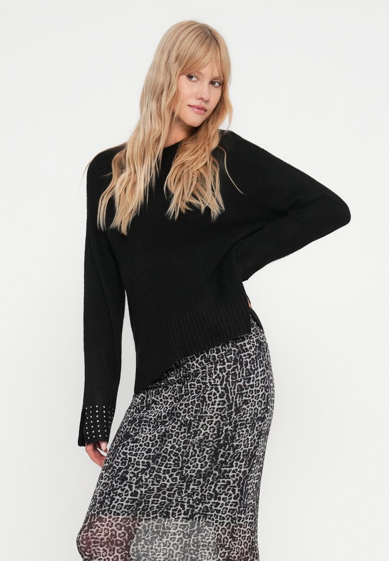 Maglione nero a maglia con orlo a coste, dotato di maniche lunghe e dettagli borchiati ai polsini, abbinato a una gonna con stampa leopardata.