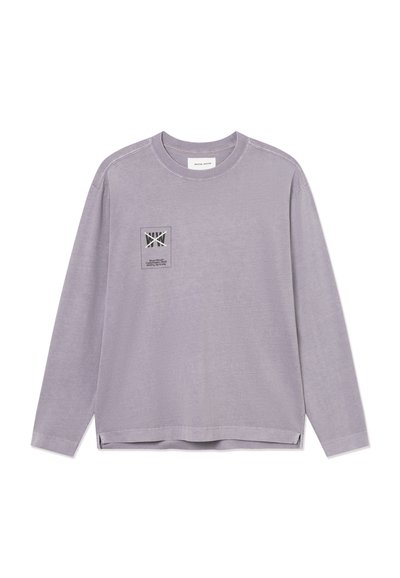 Chemise lavande à manches longues avec encolure ronde et petite étiquette logo imprimée sur le côté gauche de la poitrine, présentant des éléments de texte et graphiques.
