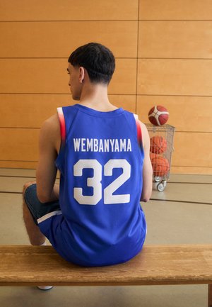 Blue basketball jersey with white number "32" and name "WEMBANYAMA" on the back. Worn with denim shorts, sitting on a wooden bench.