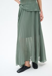 Faltender Maxirock aus weichem, hellgrünem Stoff; mit einem fließenden Design und einem geschichteten Saum. Kombiniert mit schwarzen Slippers.