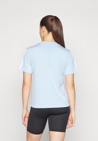 Camiseta de manga corta azul claro con cuello redondo, que presenta detalles blancos en los hombros. Material de algodón suave. Pantalones cortos negros visibles.