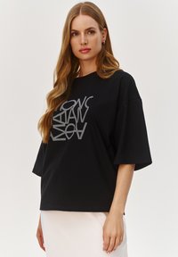 Czarna bawełniana koszulka z krótkim rękawem i luźnym krojem, z kontrastującym graficznym wzorem na przodzie w kolorze srebrnym.