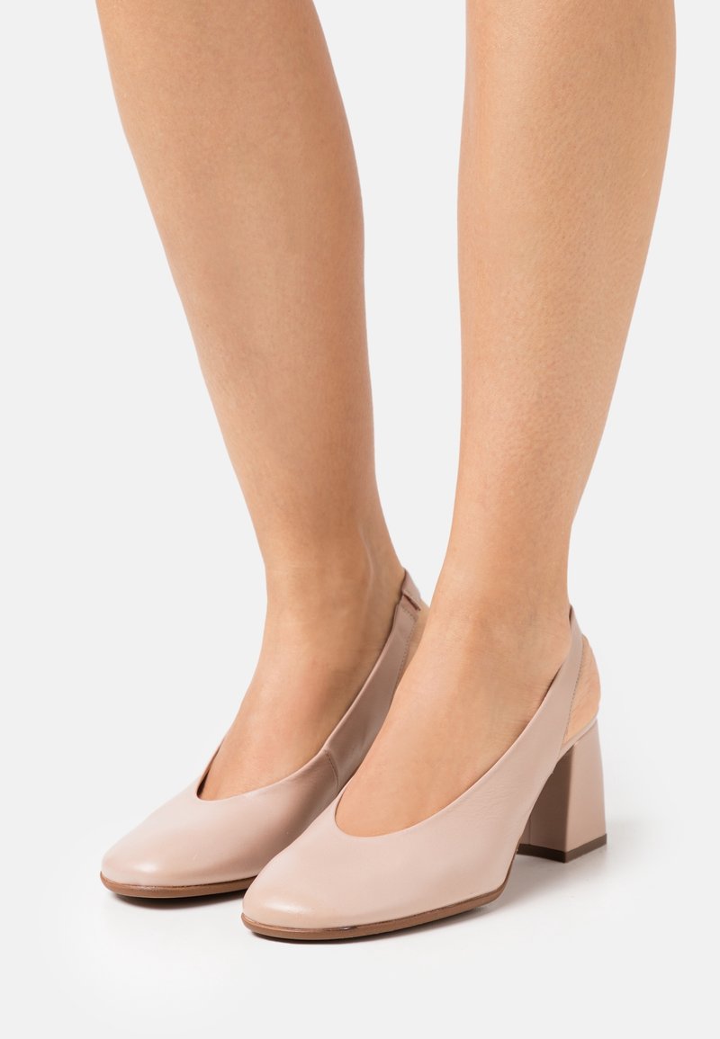 Femme portant des chaussures slingback en cuir rose clair à talon bloc et bout fermé sur fond blanc.