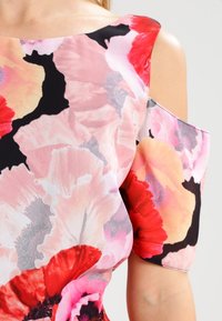 Robe courte à manches courtes à motifs floraux, présentant un mélange de fleurs rouges, roses et pêches sur fond noir, fabriquée en tissu léger et lisse.