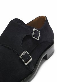 Chaussure habillée en daim noir à double boucle monastique avec boucles argentées, bout arrondi et talon empilé bas.